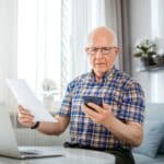 Worried senior male checking bills using laptop at home