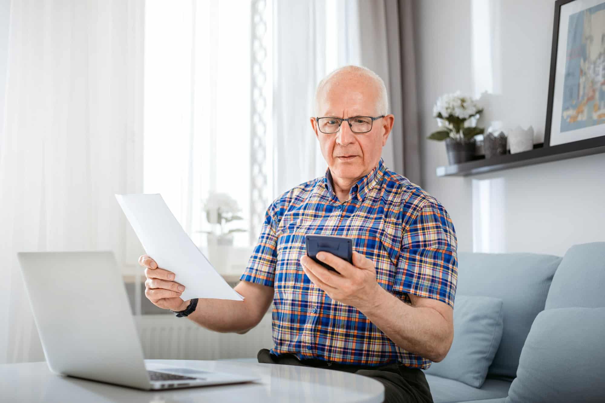 Worried senior male checking bills using laptop at home